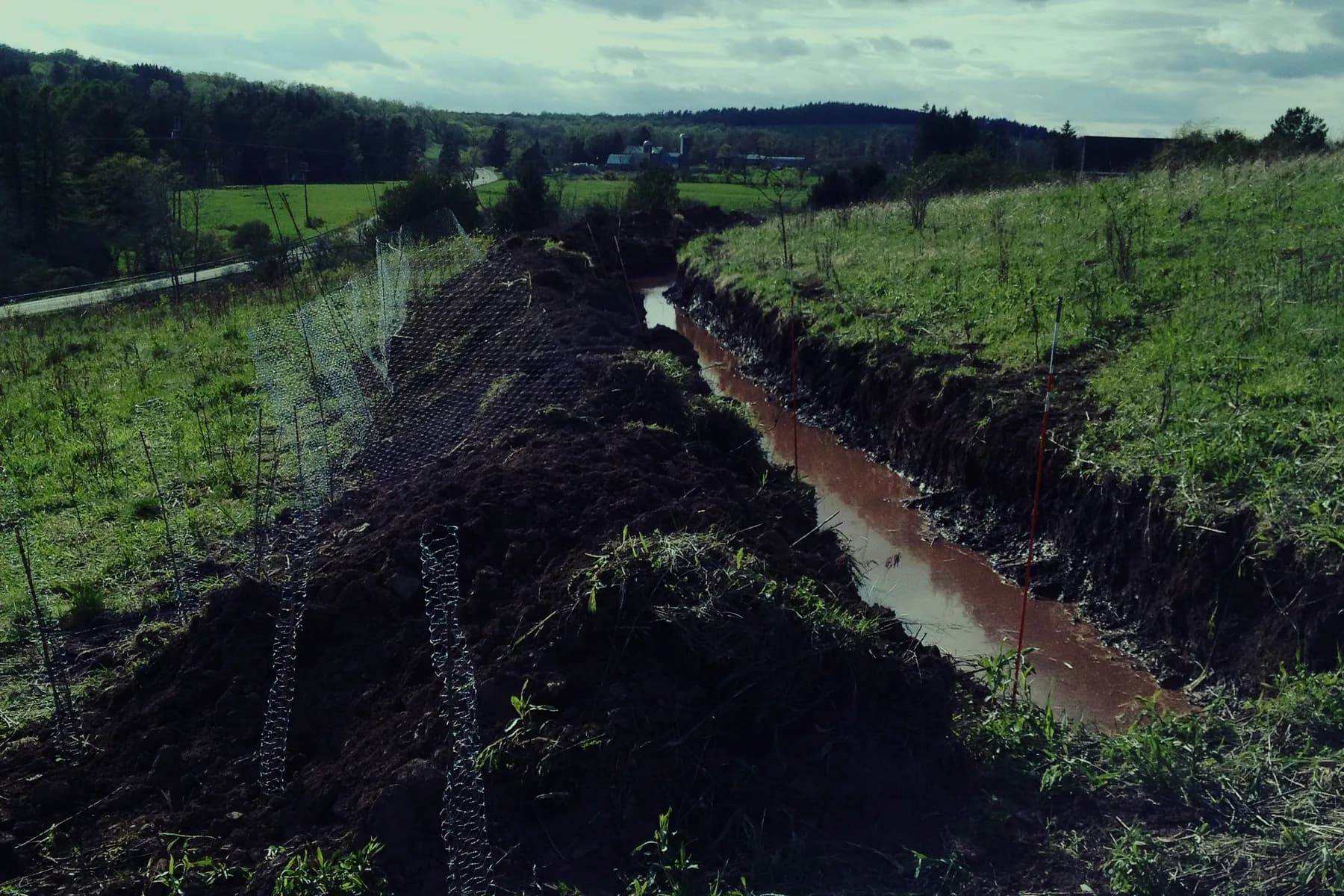 A freshly dug swale cutting across a green field